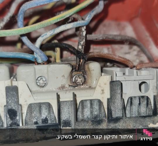 חוטי חשמל צבעוניים מחוברים לקופסת חיבורים עם סימני שריפה